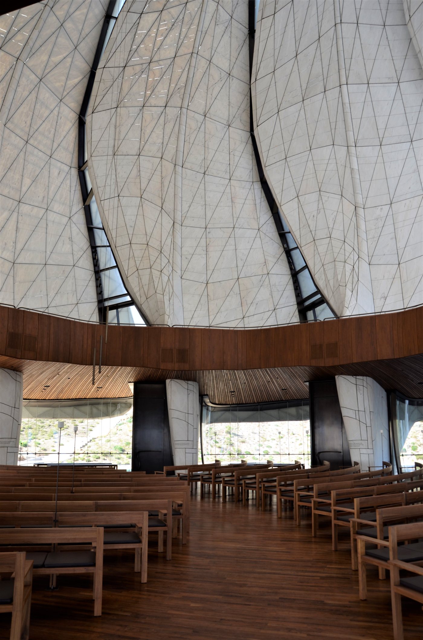 Interior del Templo Bahá’í: las alas de mármol translúcido se elevan sobre las bancas de madera y los espejos de agua