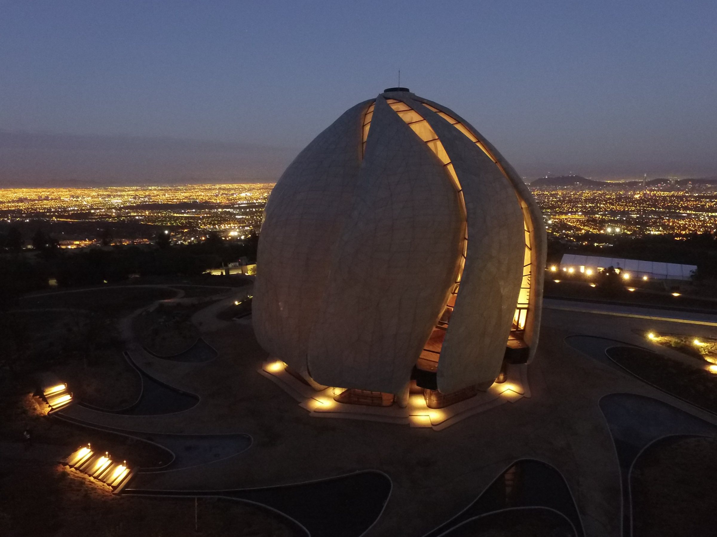 Vista aérea del Templo Bahá’í iluminado al anochecer sobre las luces de Santiago